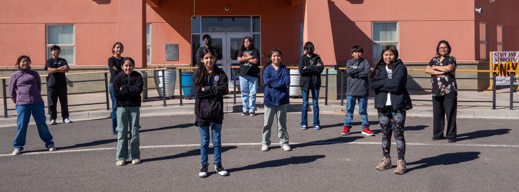 Several students and their teacher gathered outside in front of school, posing for a photo together.