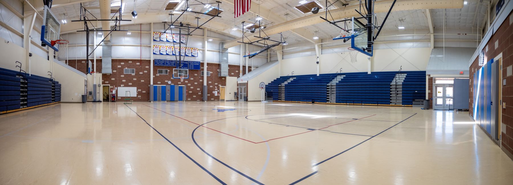 A spacious gymnasium featuring blue bleachers and a well-marked basketball court in the center.